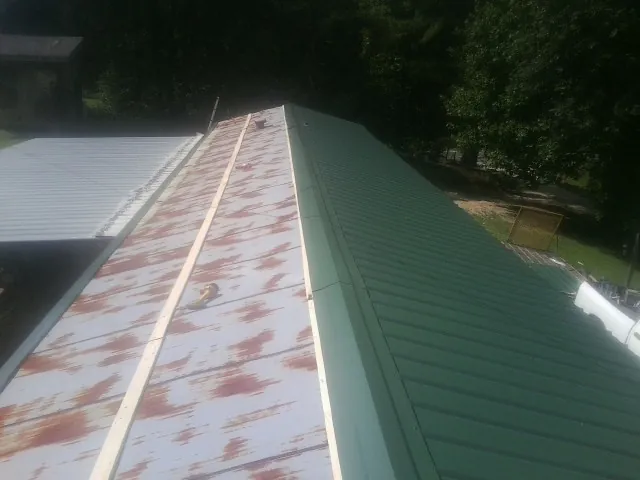 Old rusted panels beside newly installed green metal roofing — Wind Damage Roof Repair by Roofing Brothers in Putnam