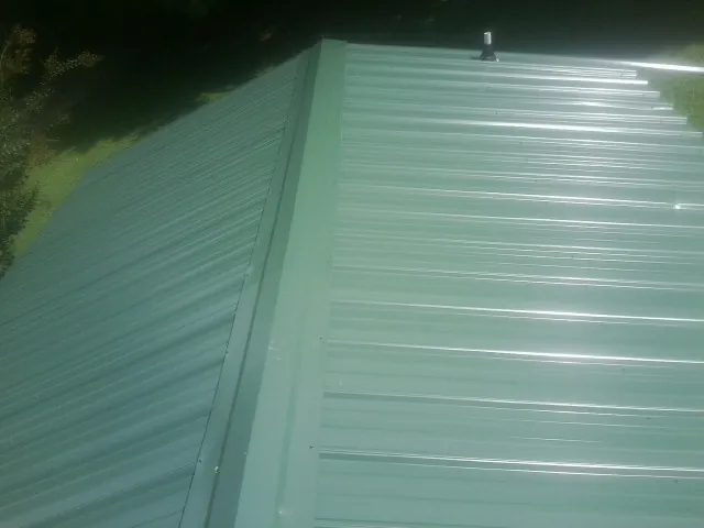New green metal panels meeting at the ridge of a roof — Flat Roof Repair work by our crew in Putnam