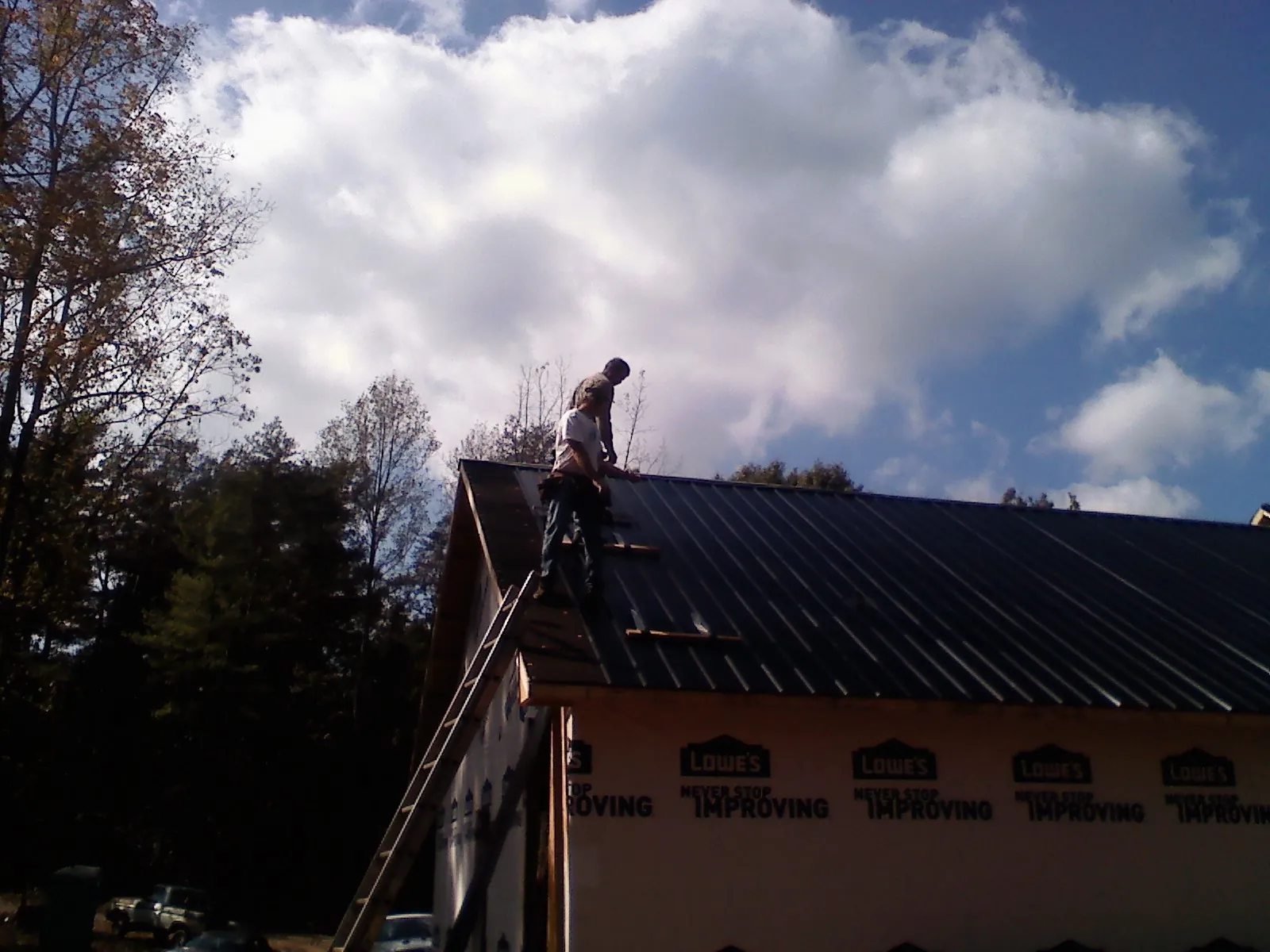 Roofer fastening dark metal panels high against a cloudy sky, from a Roof Inspection job in Putnam